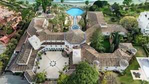 Vue aérienne d’un complexe hôtelier doté d’une piscine centrale, de plusieurs bâtiments et d’un environnement verdoyant.