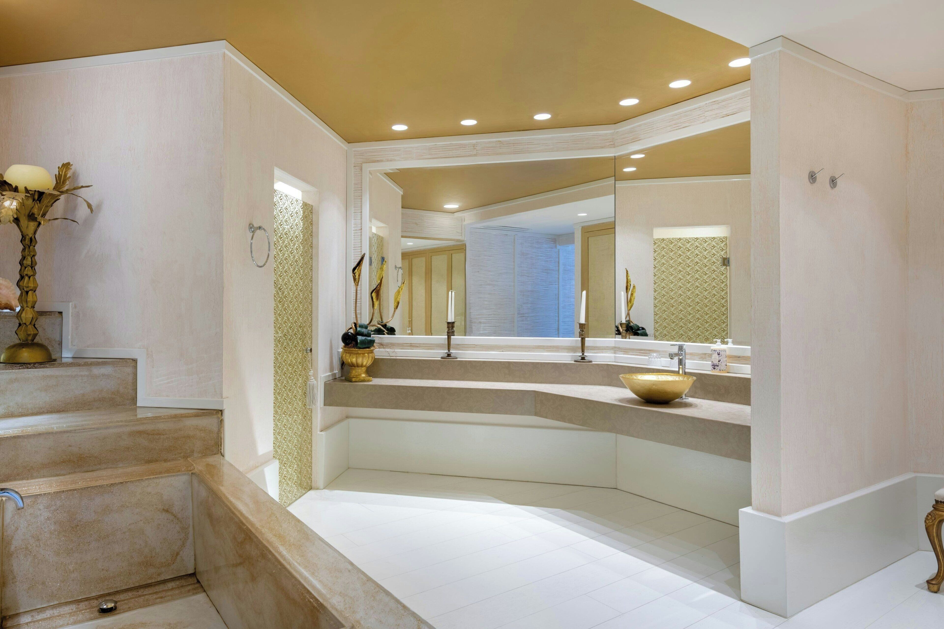 A bathroom with a large mirror, a bathtub, and a sink with a gold vessel.