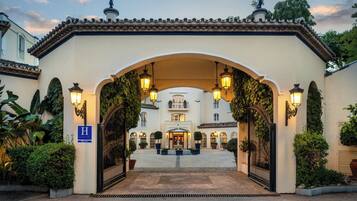 Una entrada de hotel con un arco portón, un letrero que indica un hotel y un jardín bien cuidado.