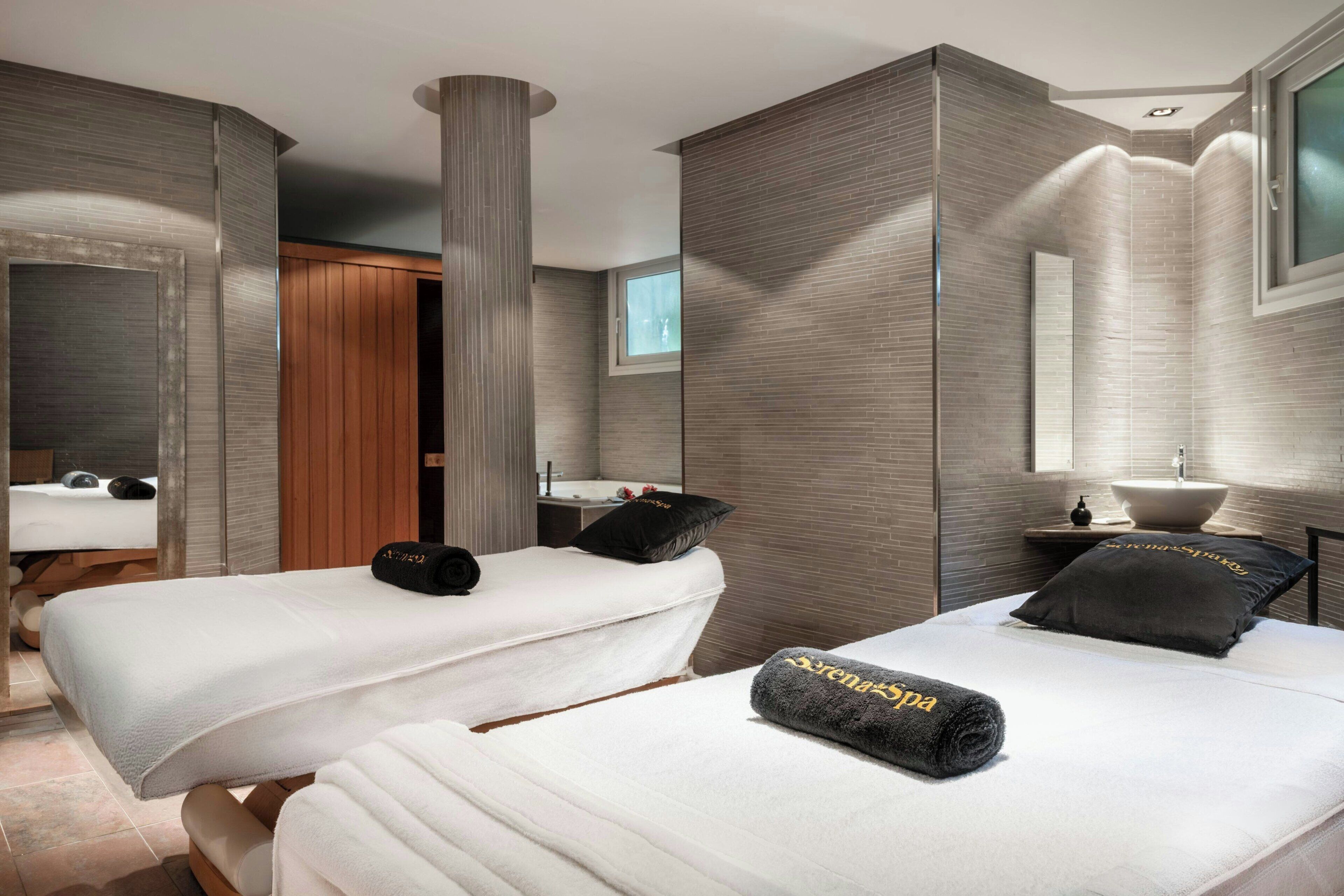Ett modernt hotellrum med två sängar, en stor spegel, ett fönster och ett handfat.