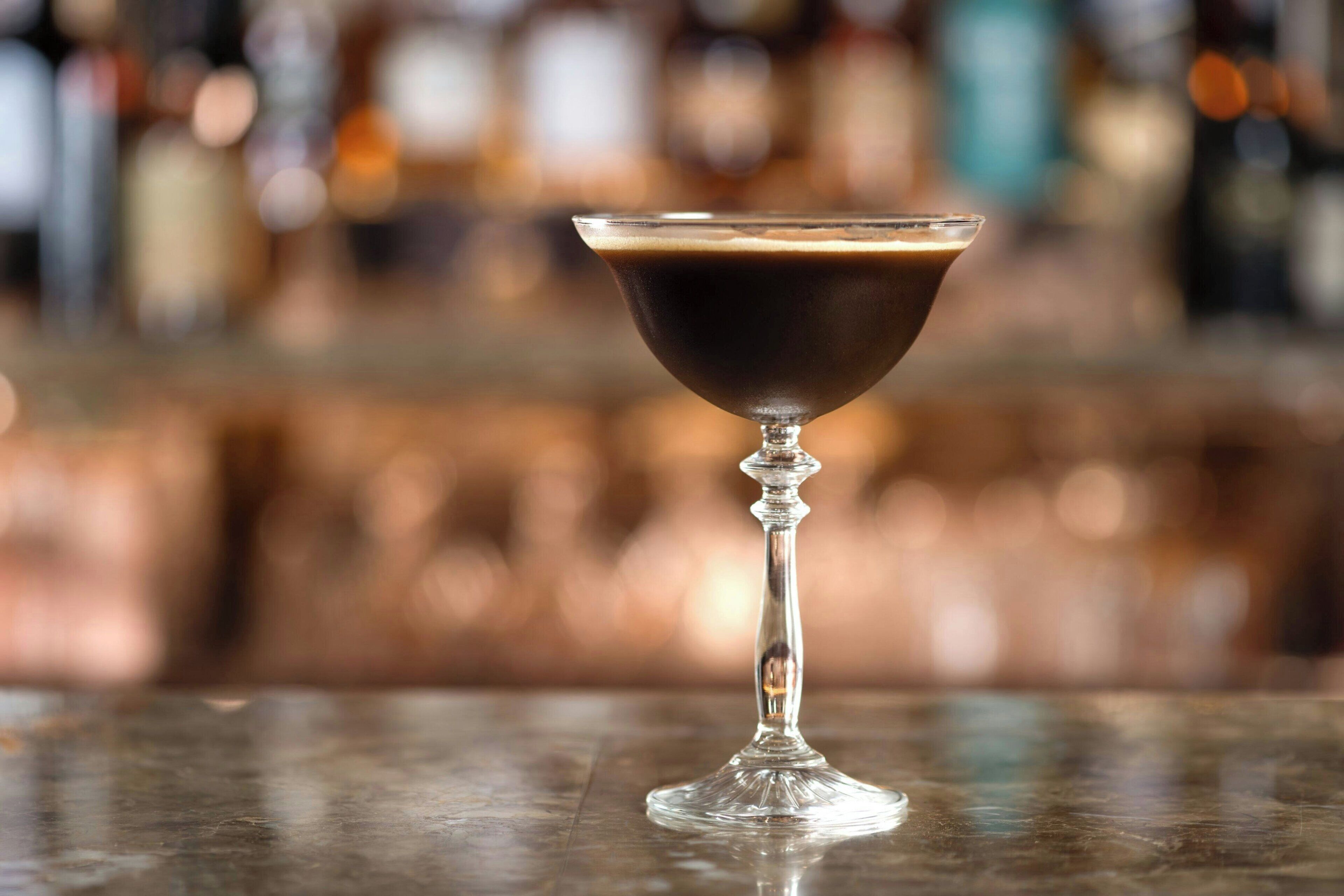 A martini glass on a bar counter with a blurred background of bottles.