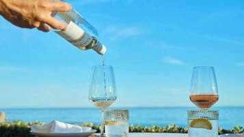 A hand pouring a clear liquid into a glass, with a view of the sea in the background.