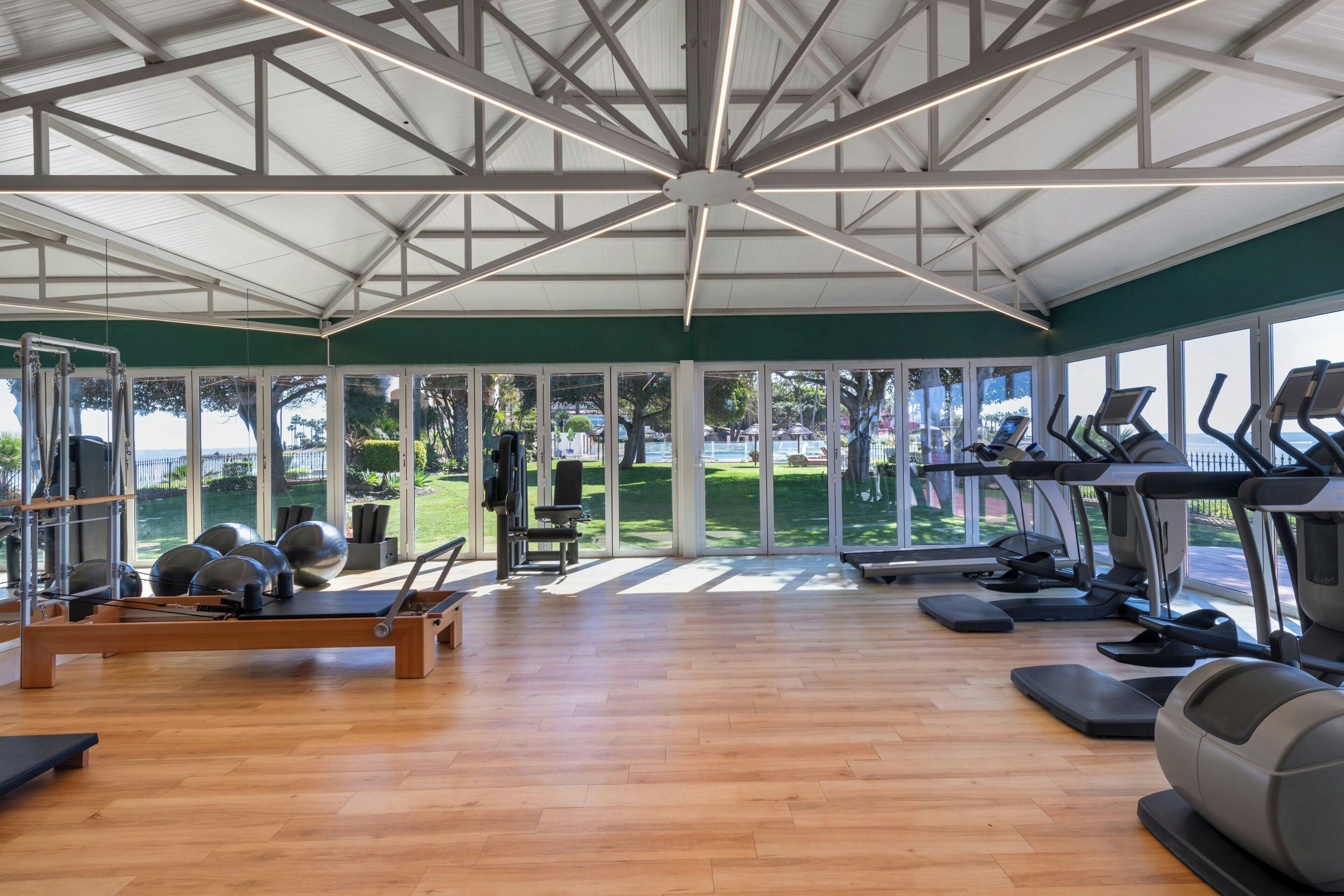 Un gimnasio con equipo de ejercicio, amplias ventanas y suelo de madera.