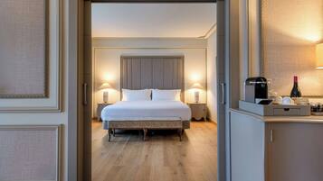 Habitación de hotel con cama, lámparas de noche, mesita de noche, cafetera y una botella de vino.