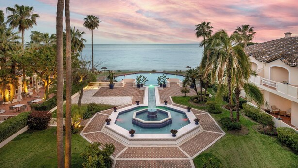 A resort with a central fountain, palm trees, a pool, and a view of the ocean. - Grand Hotel Las Dunas, Autograph Collection (Estepona)