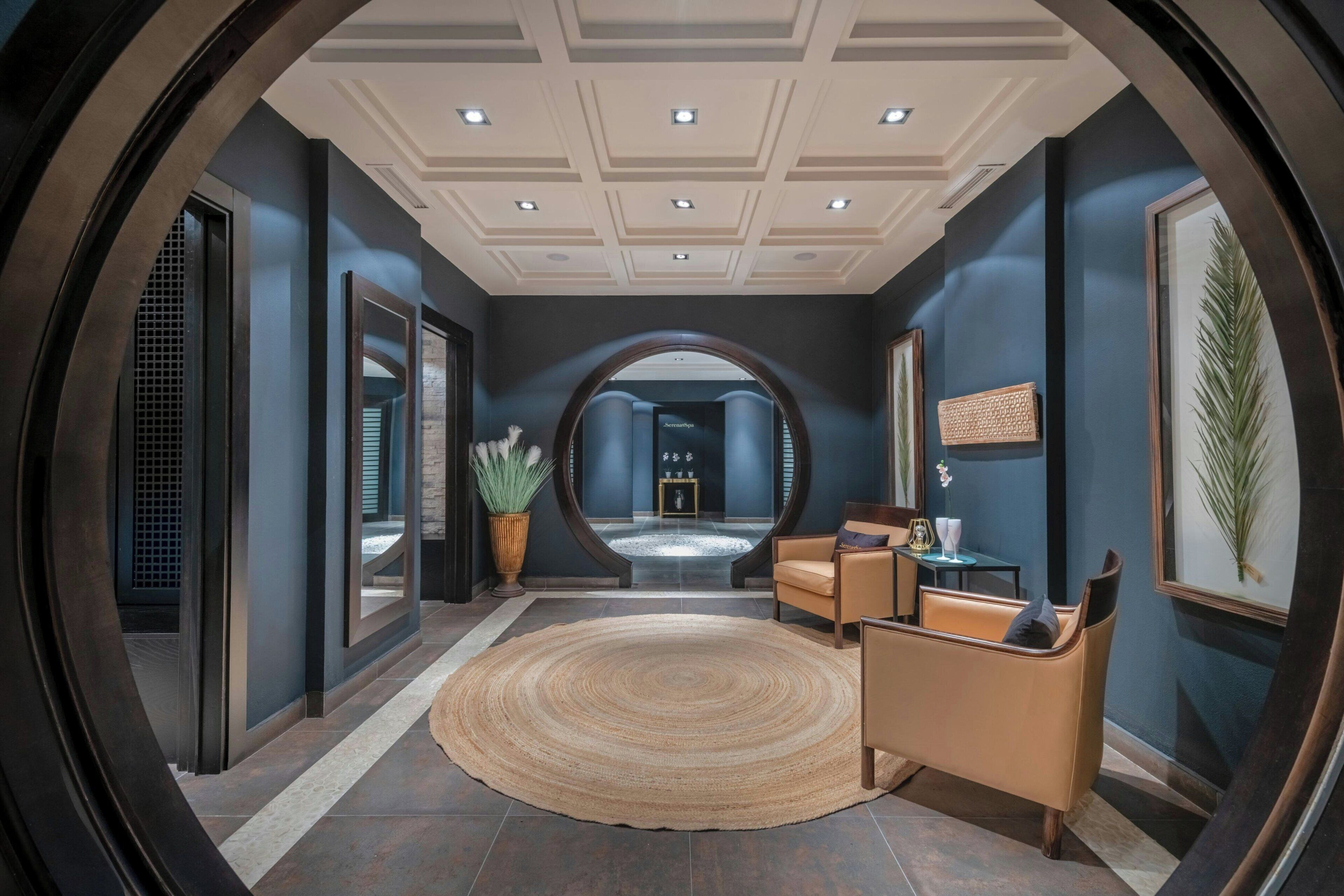 A modern lobby with a round rug, leather chairs, and a large mirror.