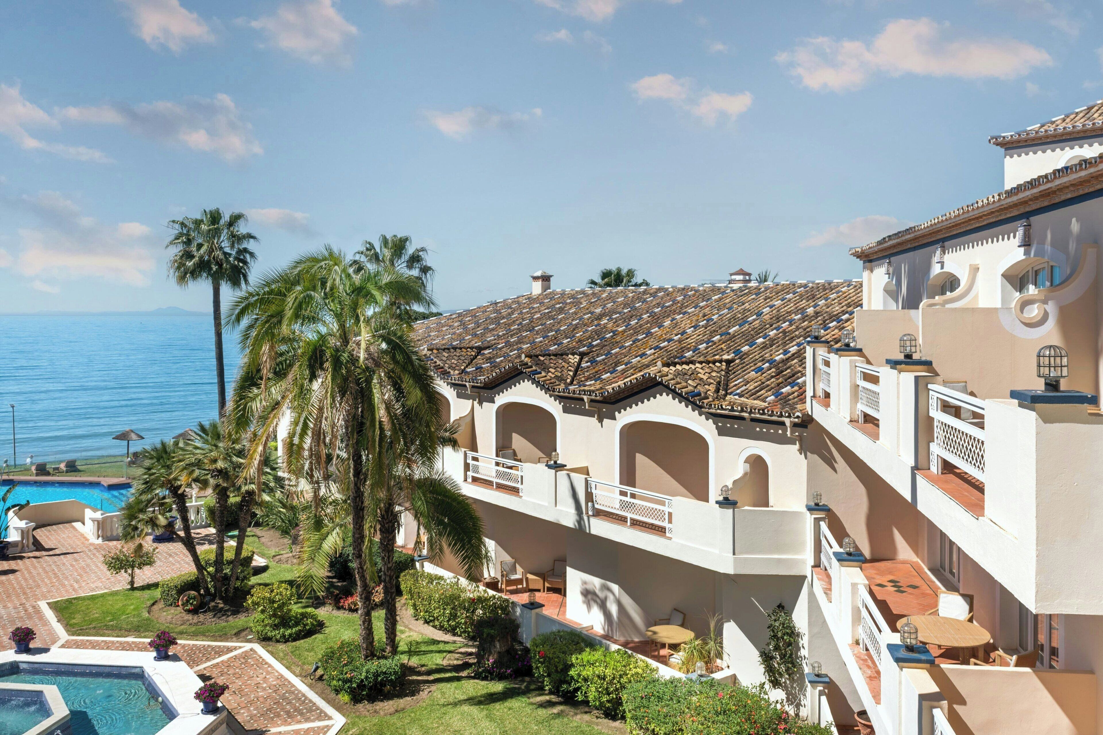 A resort with a pool, palm trees, and a view of the ocean.