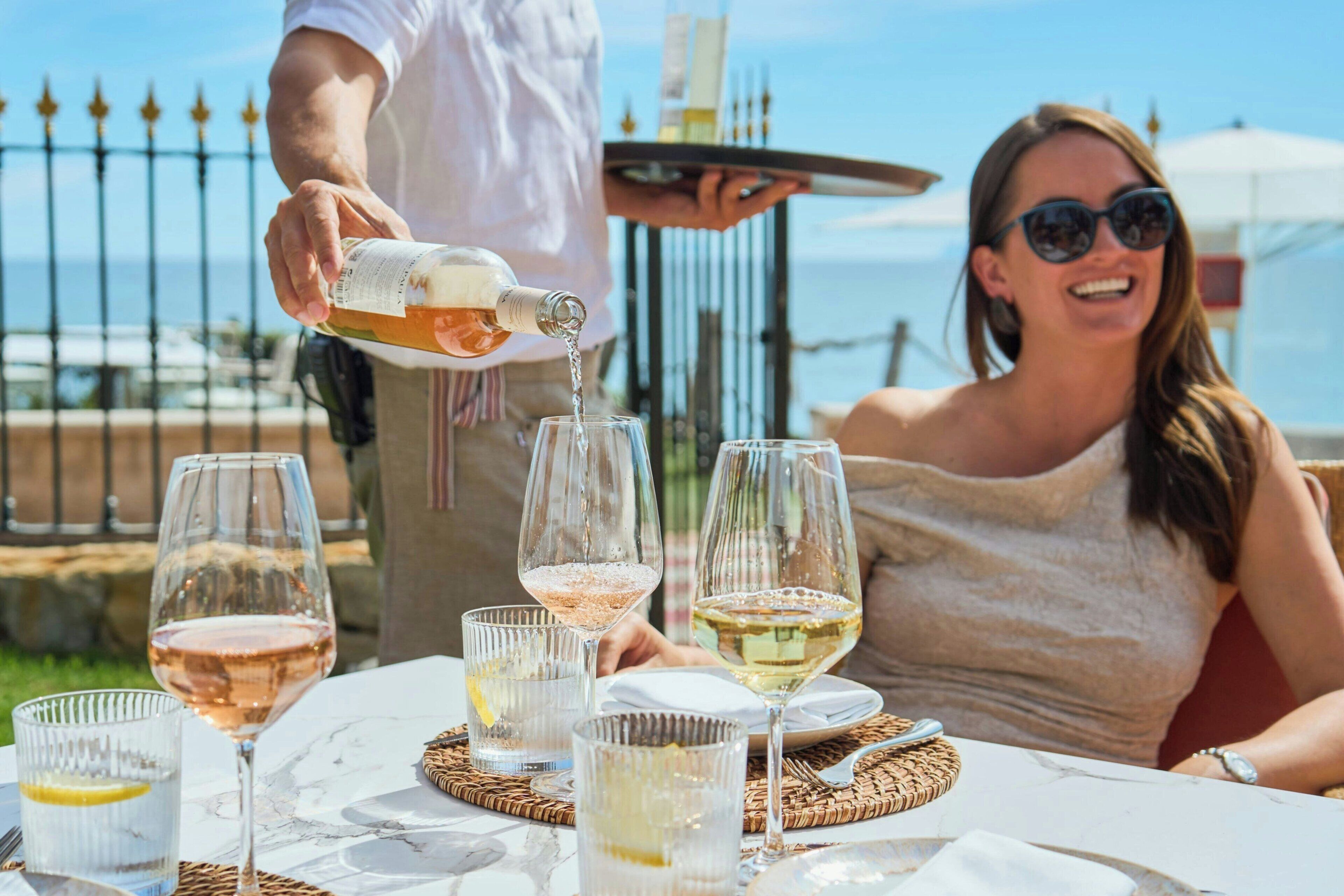 Una mesa con varias copas de vino, una botella sirviéndose y una persona sirviendo.