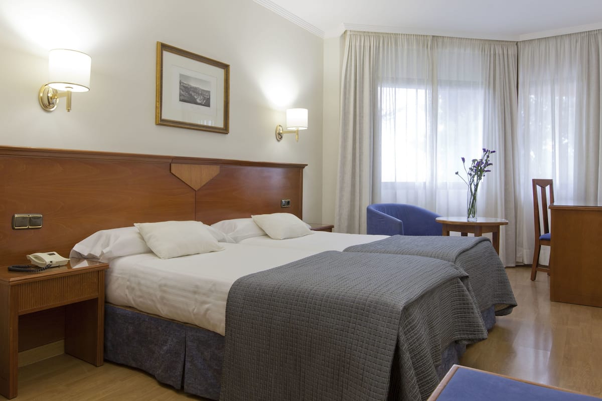 A hotel room with two beds, a desk, a chair, and a window with curtains.