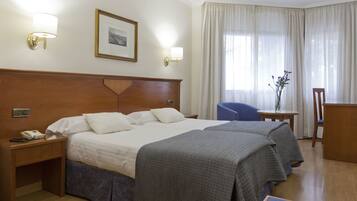 Habitación de hotel con dos camas, un escritorio, una silla y una ventana con cortinas.
