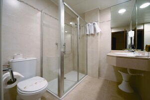A bathroom with a glass-enclosed shower, a toilet, and a sink with a mirror above it.