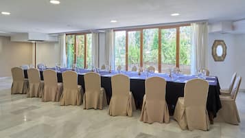 Un salón de conferencias con una larga mesa, sillas color beige y grandes ventanales con cortinas.