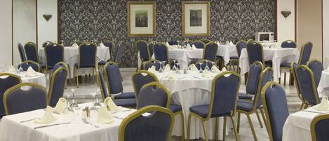 Un salón de banquetes con mesas redondas, sillas tapizadas en azul y manteles blancos.