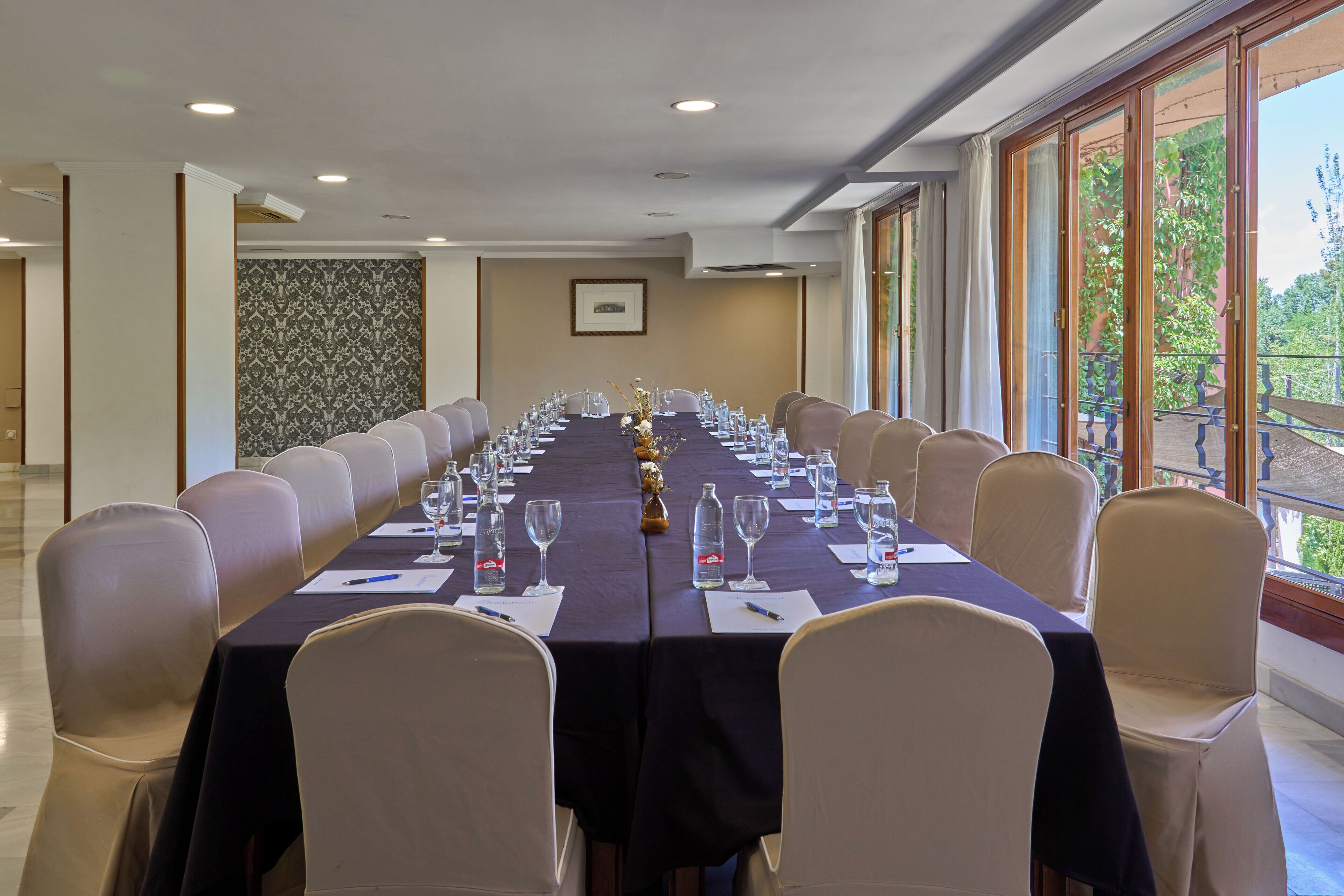 A conference room with a long table, chairs, and a view of greenery outside.