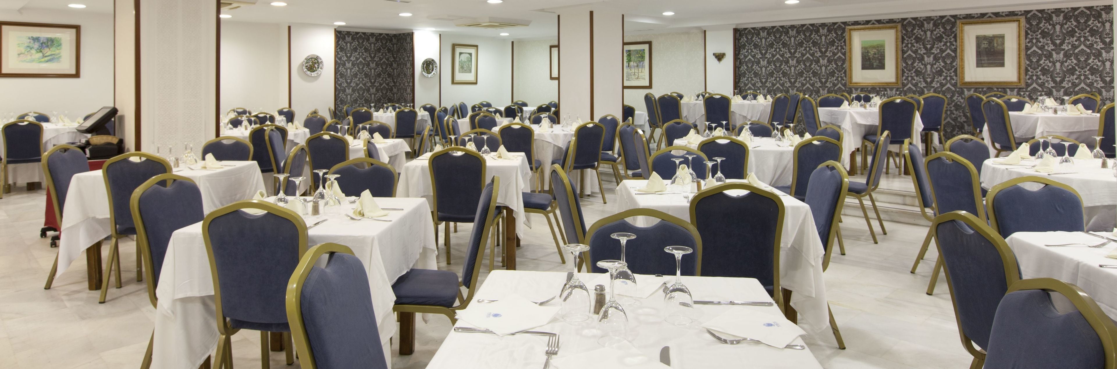 Un salón de banquetes con varias mesas redondas, cada una cubierta con manteles blancos, sillas azules y cubiertos.