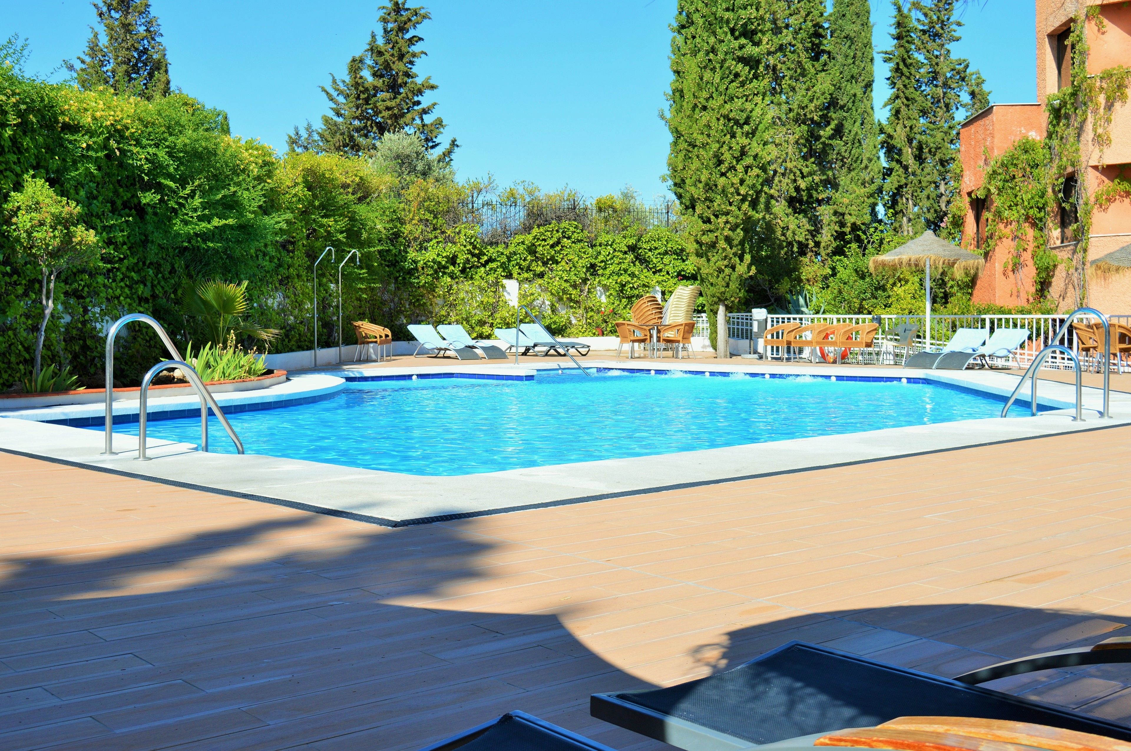 A rectangular swimming pool with clear blue water, surrounded by a wooden deck. There are lounge chairs and a small table with umbrellas.