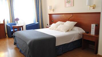 Habitación de hotel con una cama grande, un escritorio con una silla, una mesita con un florero y una mesita de noche con una lámpara.