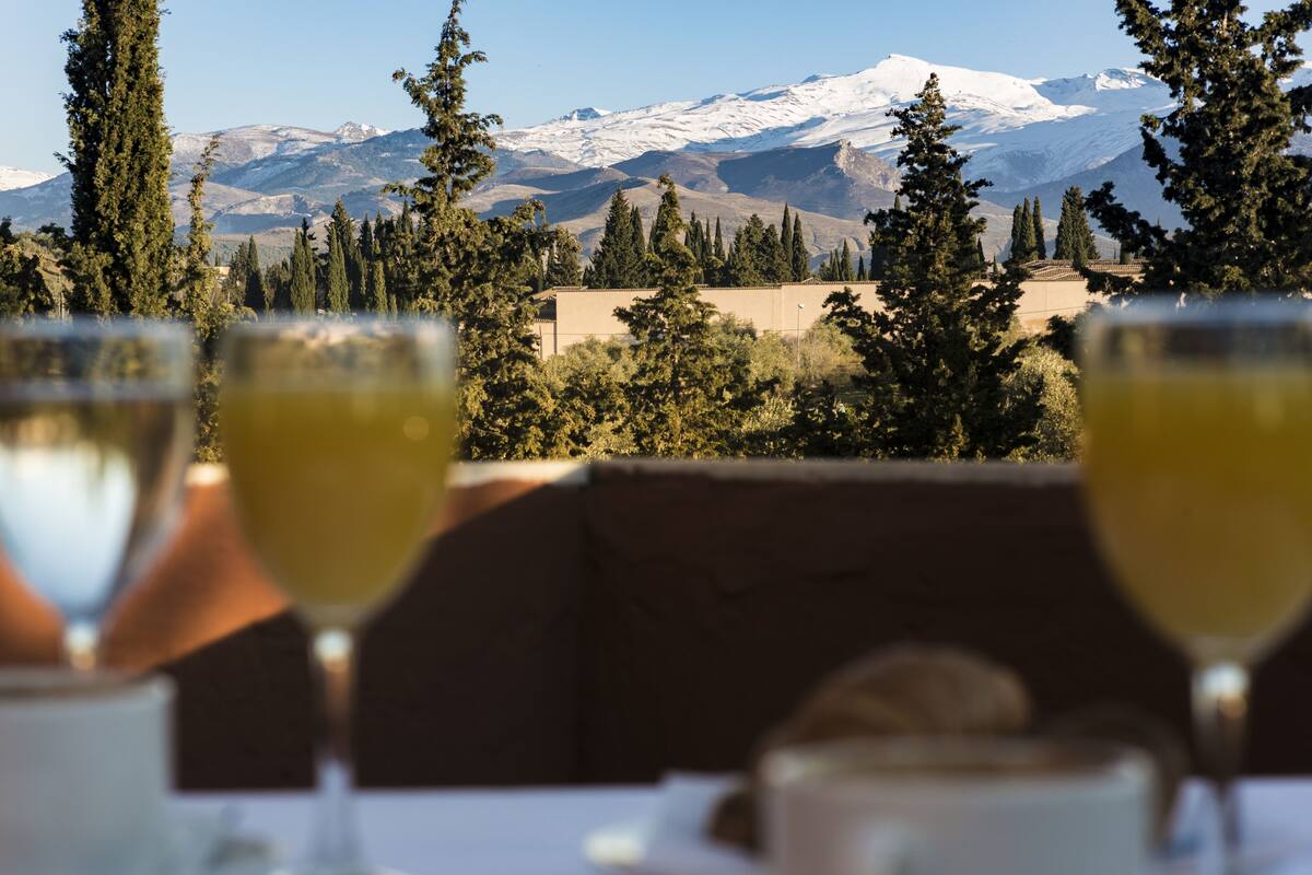 A table with two glasses of a yellow beverage, set against a backdrop of snow-capped mountains and trees.
