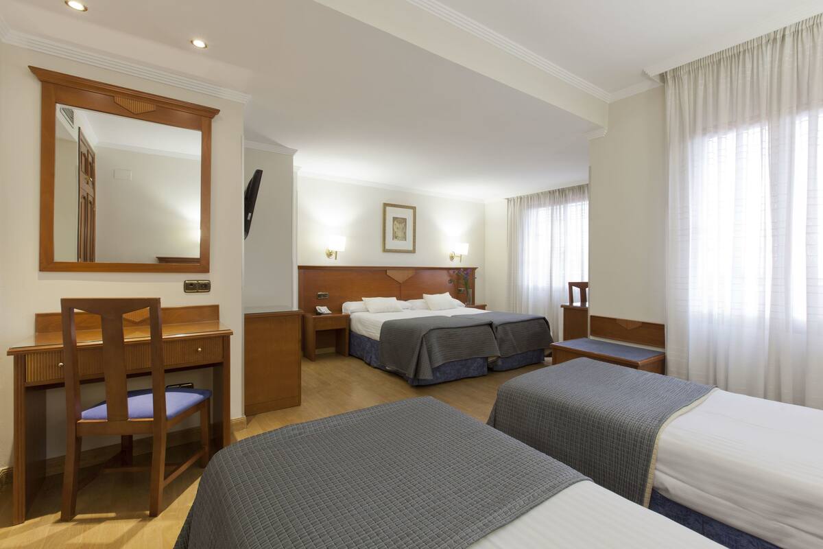 A hotel room with two beds, a desk, a chair, a dresser, and a large mirror.