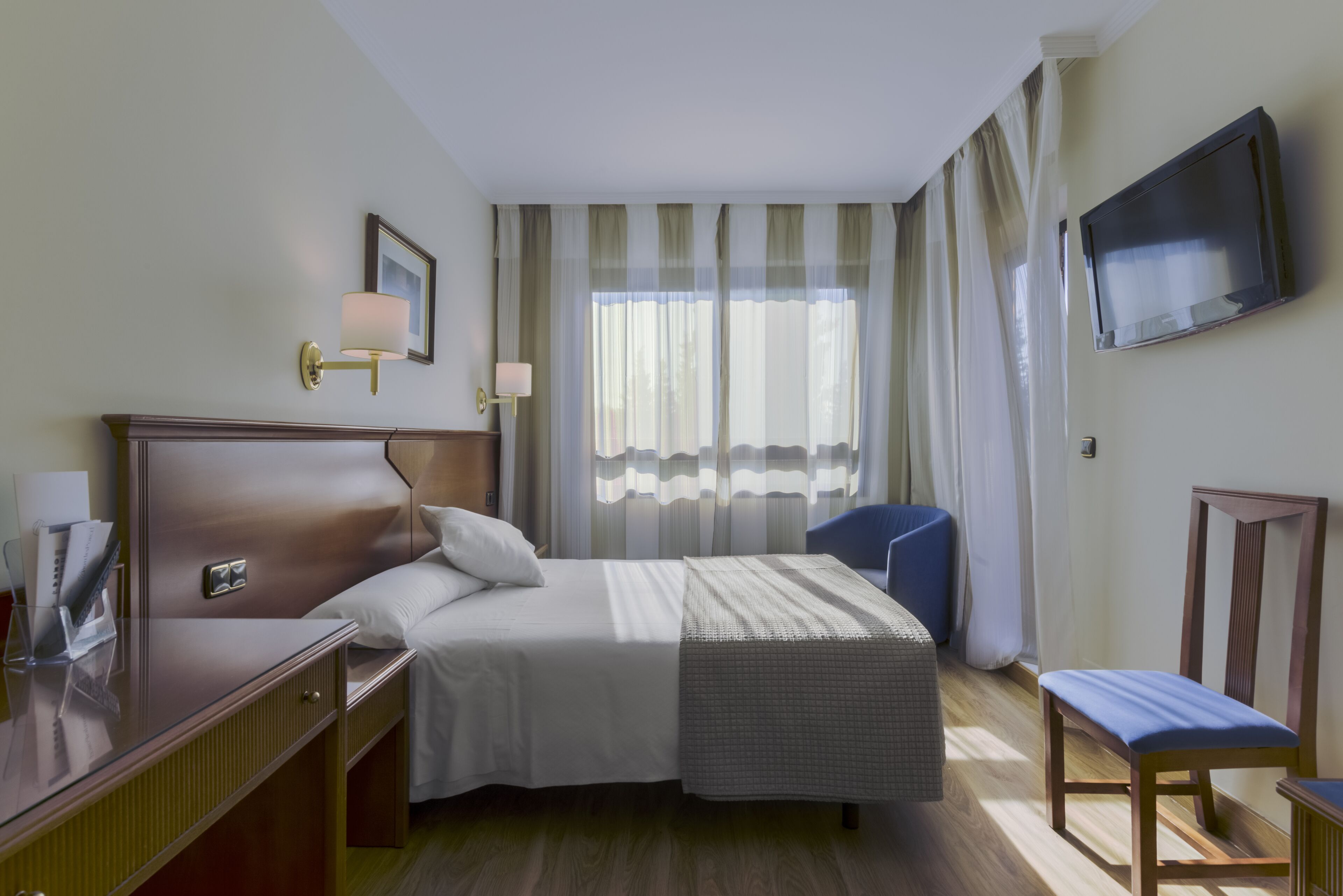 Een hotelkamer met een bed, nachtkastje, lamp, televisie en een stoel.