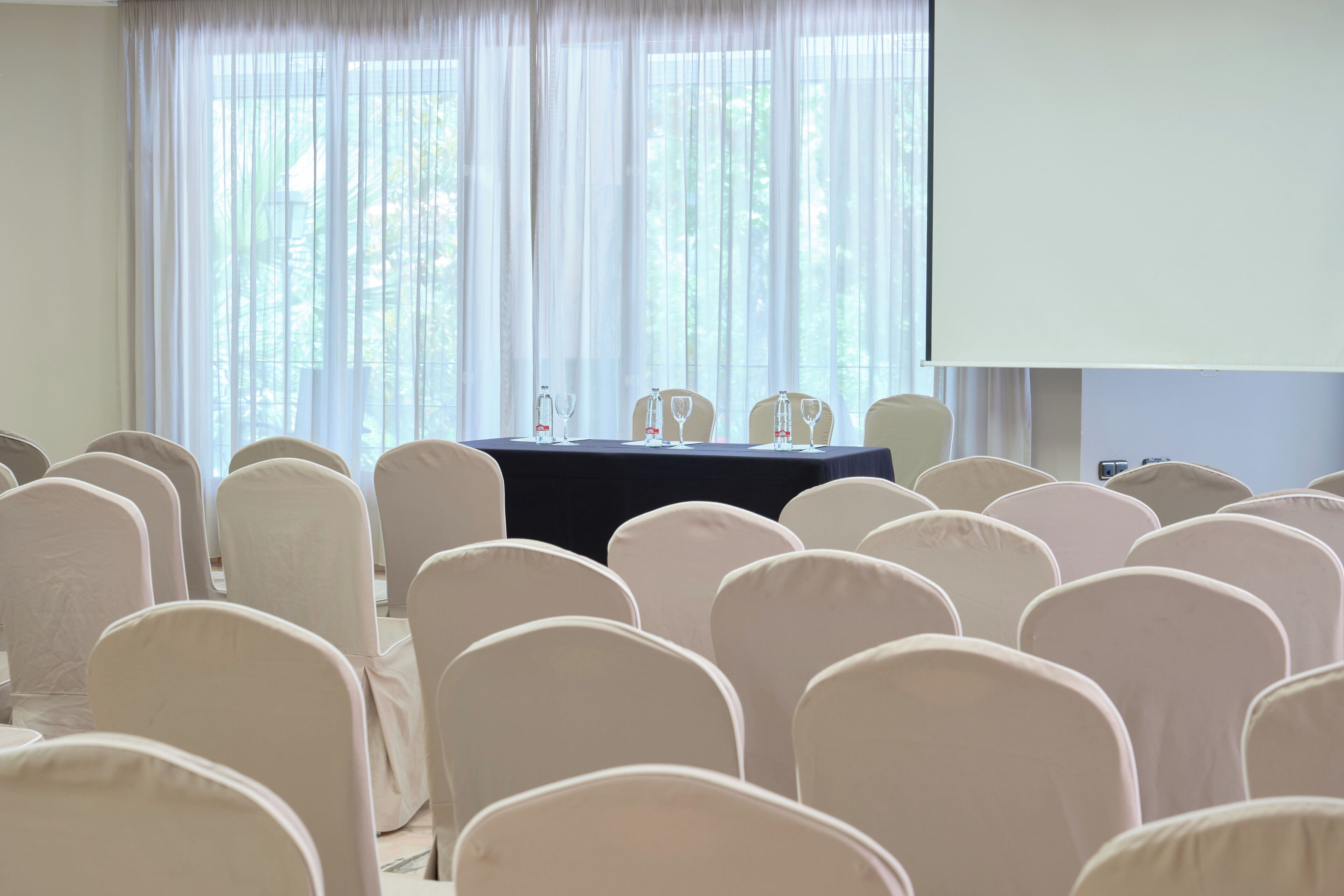 A conference room with rows of chairs and a table with a projector screen.