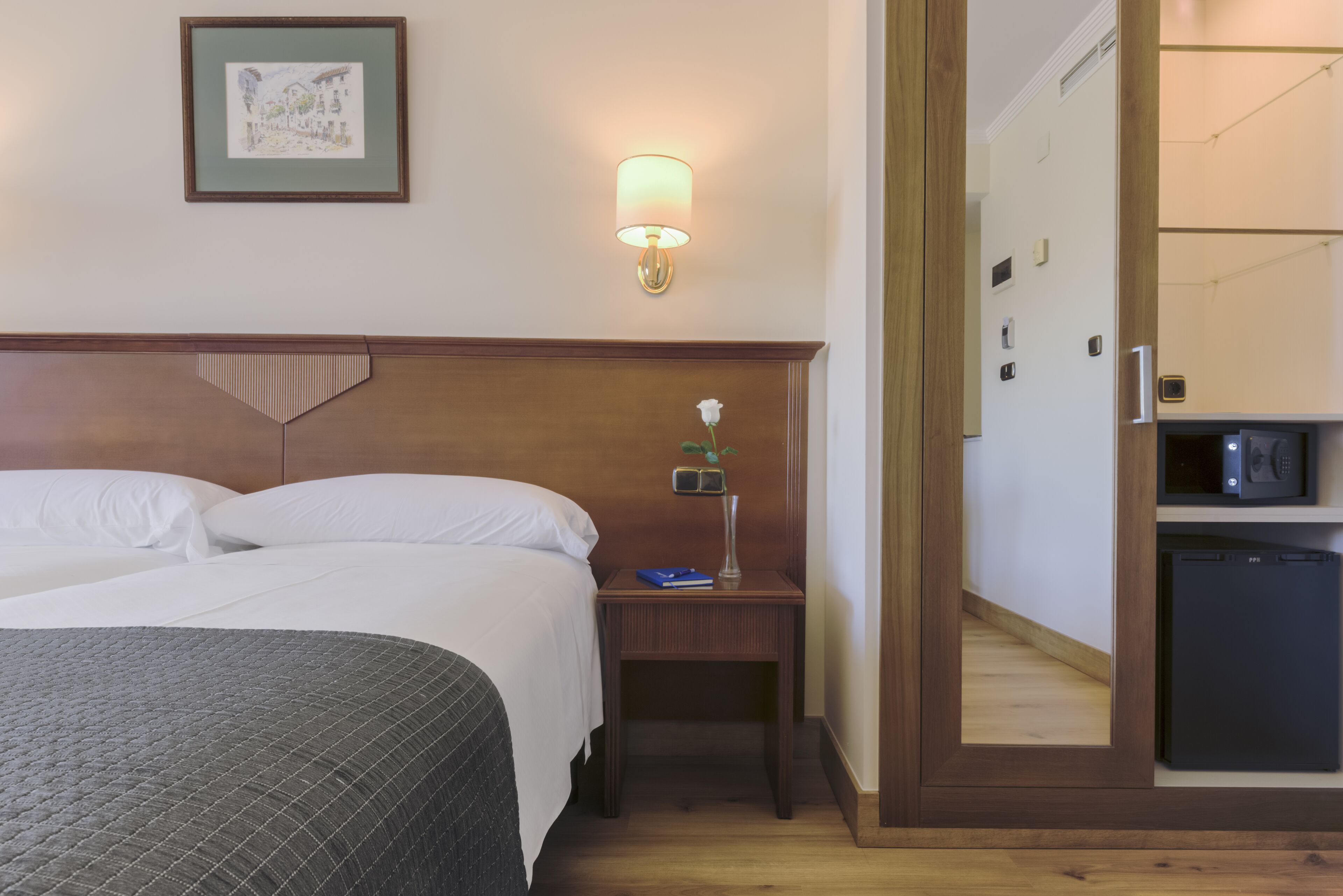 A hotel room with a bed, bedside table, lamp, and a small refrigerator.