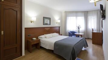 A hotel room with a wooden bed, bedside tables, a desk, a chair, and a TV mounted on the wall.