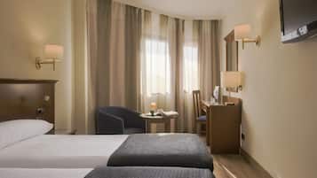 Habitación de hotel con dos camas, un escritorio, una silla, un televisor y una ventana con cortinas.