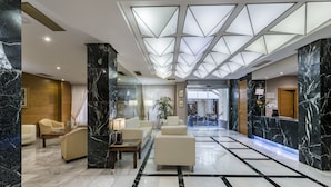 A hotel lobby with marble flooring, a reception desk, and seating areas.