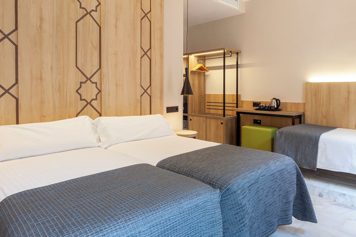 A hotel room with two beds, a desk, a chair, a mirror, and a hanging coat rack.