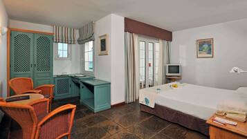 A hotel room with a bed, a desk with a chair, a television, and a window with curtains.