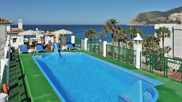 Relax by the rooftop pool with a stunning sea view, surrounded by lush greenery and comfortable lounge chairs.
