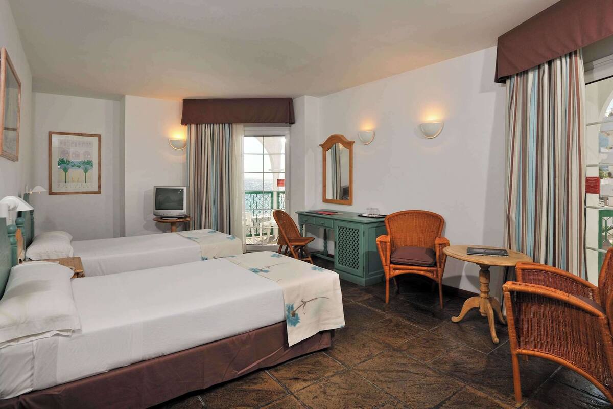 Une chambre d’hôtel avec deux lits, un bureau, une chaise, une petite table, un téléviseur et un balcon avec vue.