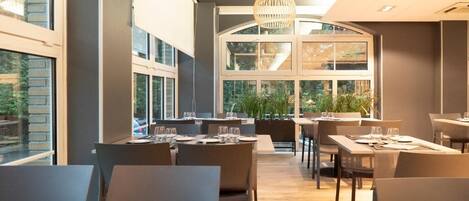 A modern dining area with tables and chairs, large windows, and a hanging light fixture.