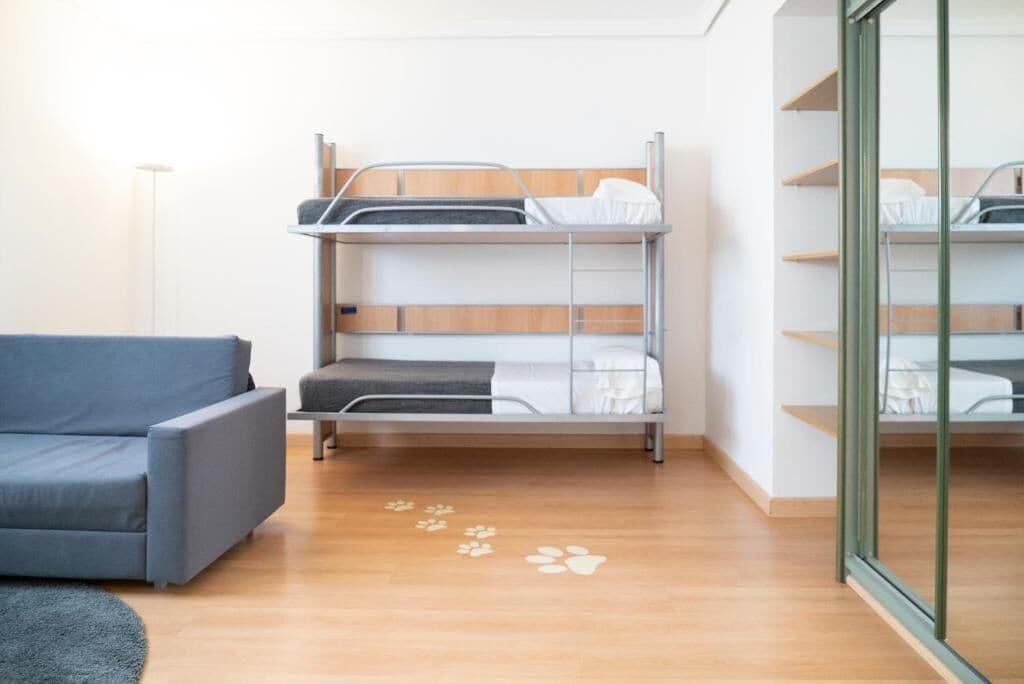 Dormitorio con literas, un sofá gris y una puerta de cristal.