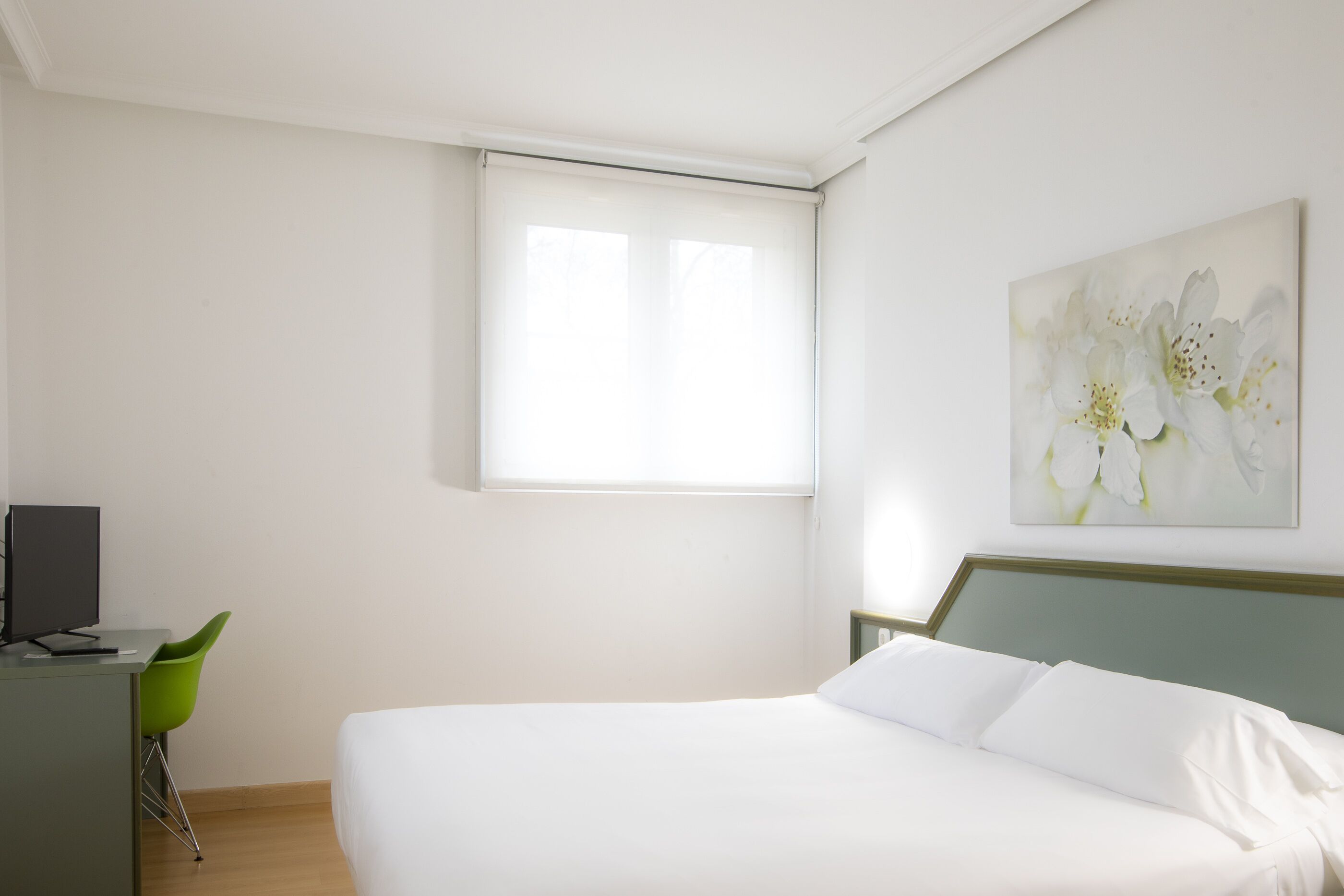 A bedroom with a bed, a desk with a computer, a green chair, and a window with blinds.