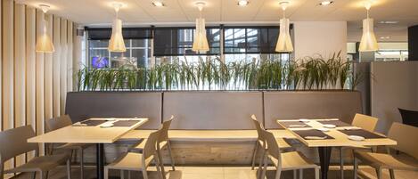 A modern dining area with multiple tables and chairs, pendant lighting, and a plant wall.