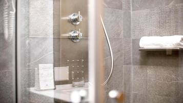 A modern shower with a glass door, a towel rack, and a glass of water on the counter.