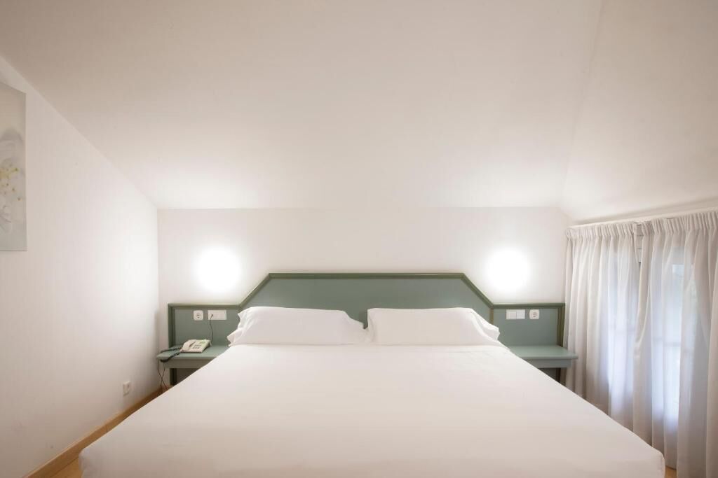 Ein Hotelzimmer mit einem Einzelbett, einem Nachttisch mit Telefon und einem Kopfteil mit Beleuchtung.