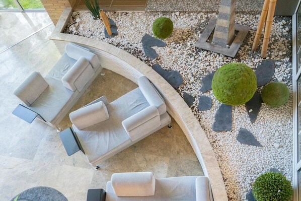 A modern outdoor seating area with a curved white sofa and chairs, surrounded by a pebble garden with green spherical bushes.
