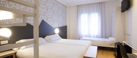 A hotel room with two beds, a desk, a chair, a TV, and a window with curtains.