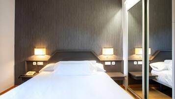 Una habitación de hotel con una cama grande, dos mesitas de noche, un espejo y lámparas de pared.