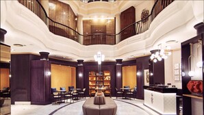 A spacious lobby with a central seating area, a reception desk, and a staircase leading to an upper level. - Occidental León Alfonso V (León)