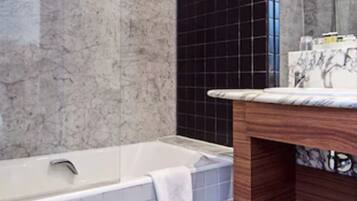 Un baño moderno con pared de mármol, una pared acento con azulejos negros, una bañera blanca y un tocador de madera.