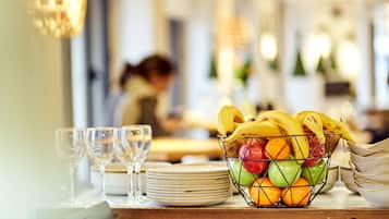 Una mesa de comedor con una cesta de frutas, copas de vino y platos apilados.