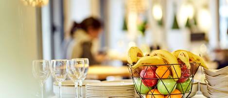 A dining table with a fruit basket, wine glasses, and stacked plates.