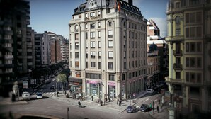 A multi-story building with a classic architectural style, featuring a prominent entrance and several ground-level retail spaces. - Occidental León Alfonso V (León)