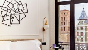 A hotel room with a bed, a wall art piece, a lamp, and a view of a building through a window. - Occidental León Alfonso V (León)