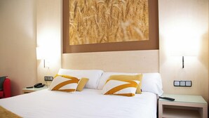 Habitación de hotel con una cama grande, dos mesitas de noche, una silla roja y un cuadro colgado en la pared.