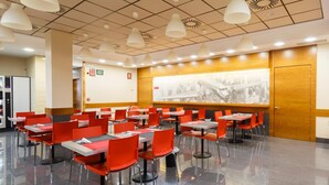 Un comedor moderno con sillas y mesas rojas, una pizarra y un mural en la pared.